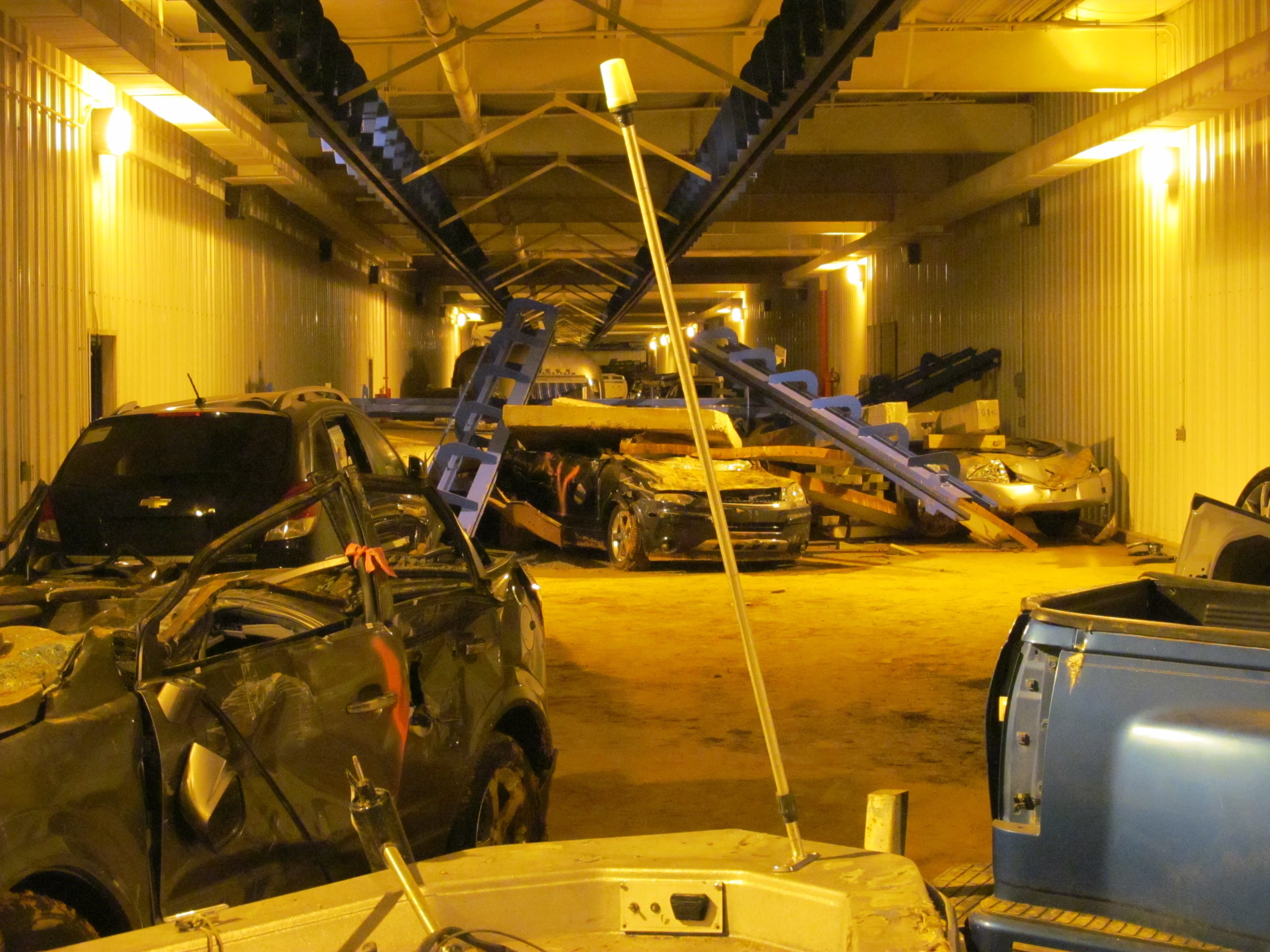 Wrecked cars and a fallen light pole fill the highway tunnel under amber lighting.