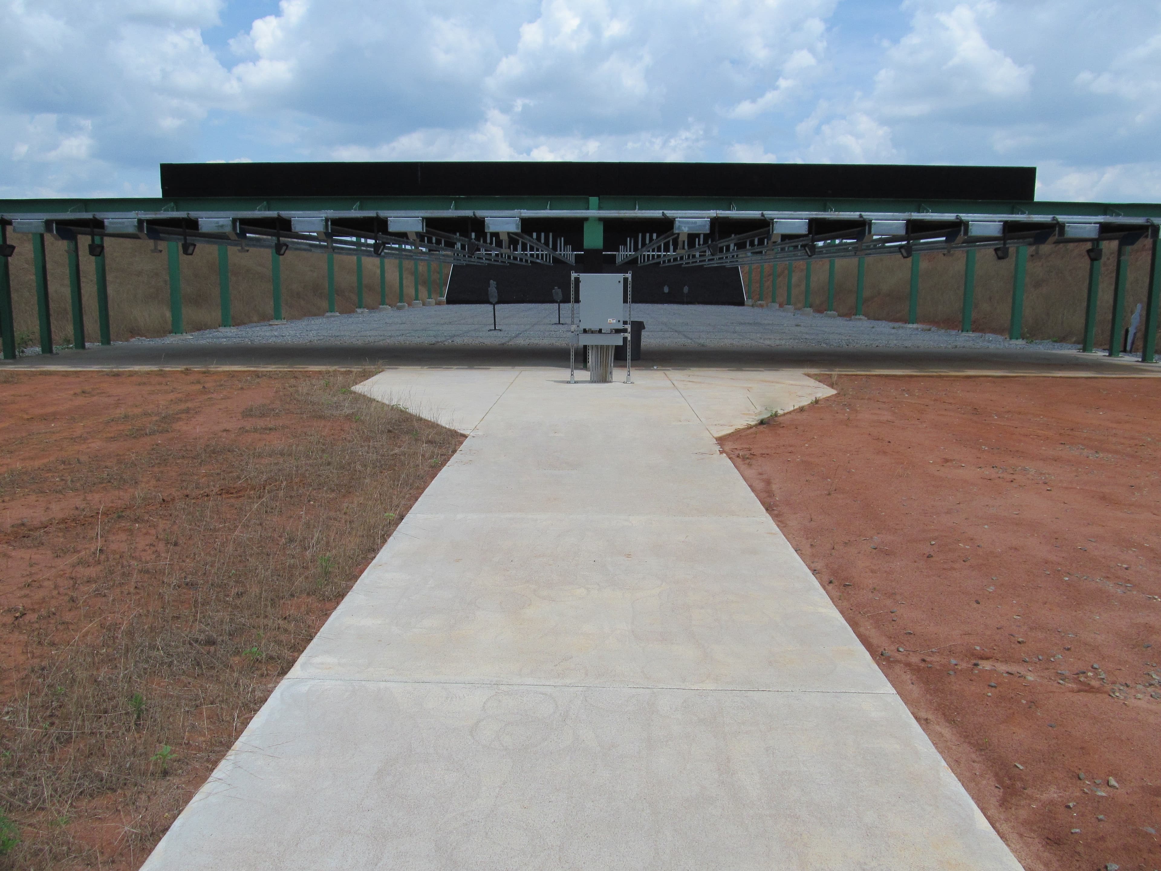 A concrete walkway leads to the covered firing line of the small arms range, target frames visible under the roof.