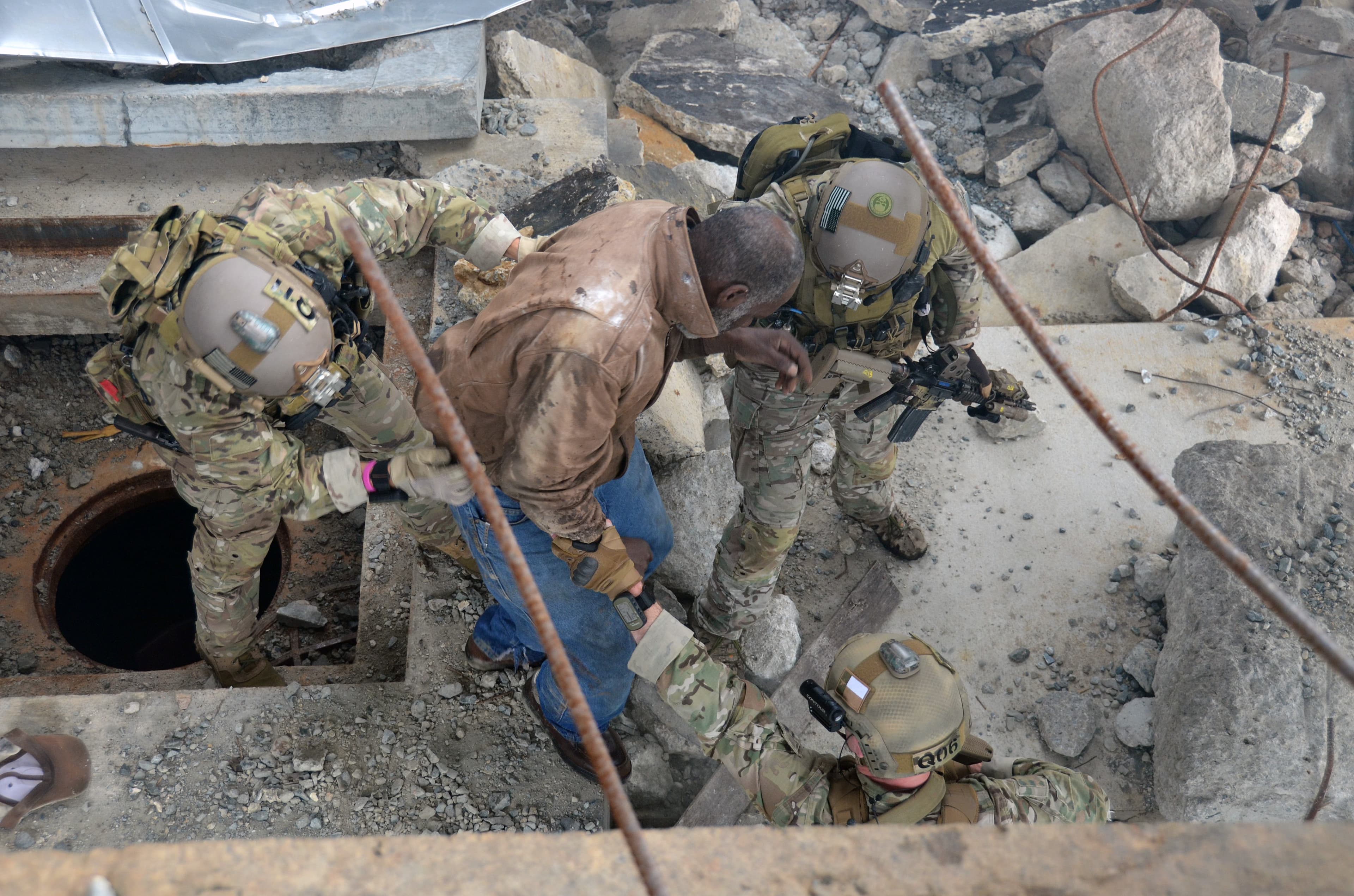 Soldiers lift a casualty out of a hole in a rubble-strewn floor during a confined-space rescue.
