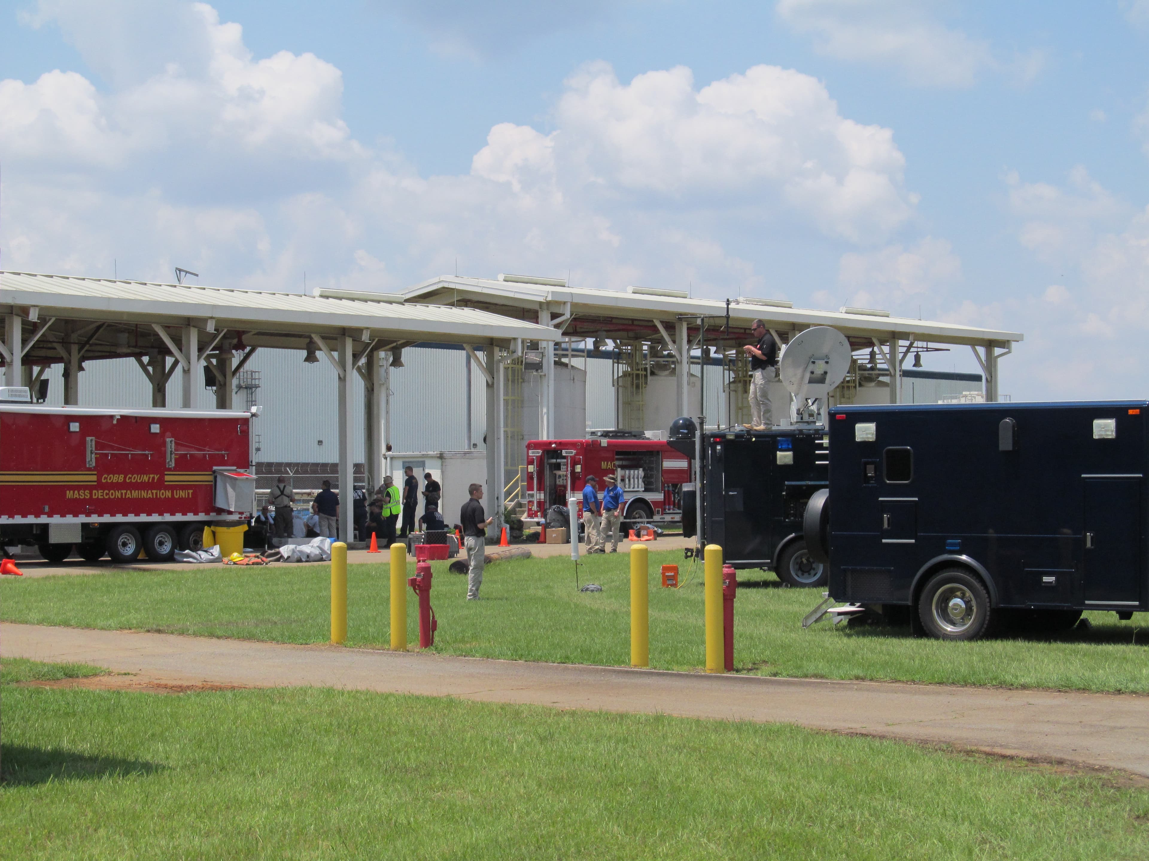 Response vehicles, including a fire engine and a trailer with a satellite dish, parked under open-sided shelters during a training event.