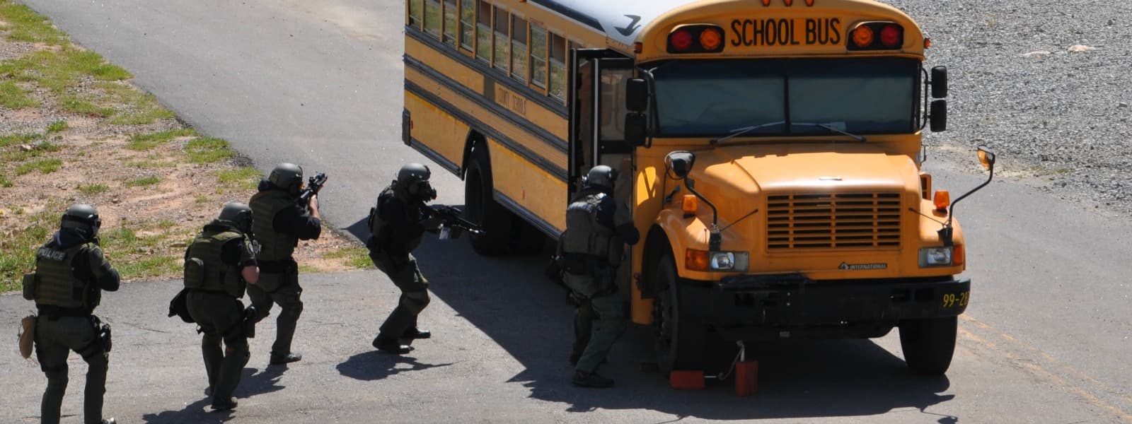 A tactical team in camouflage advances along the side of a school bus with weapons raised.