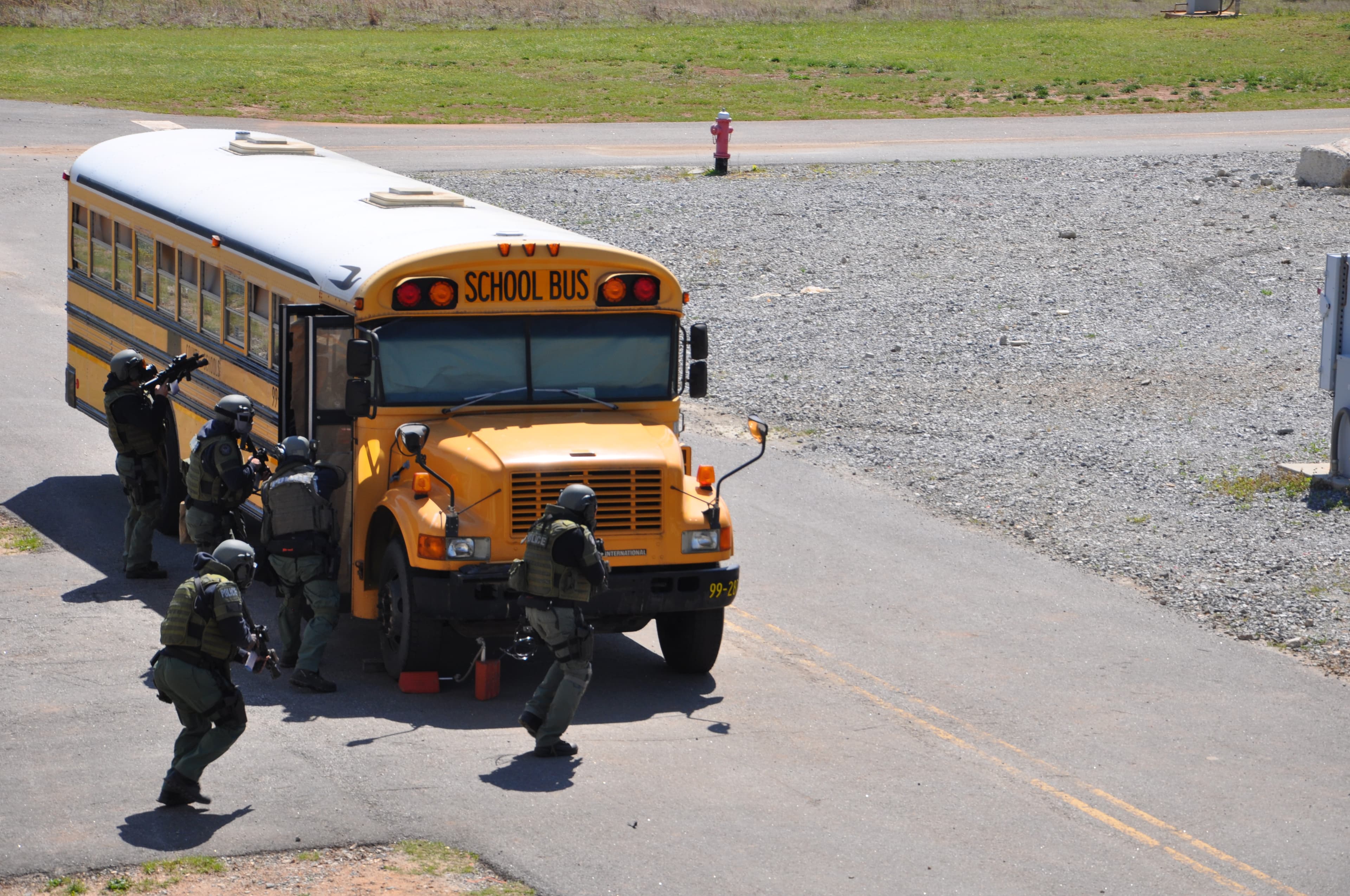 A tactical team in camouflage and helmets moves in on a school bus with weapons raised.