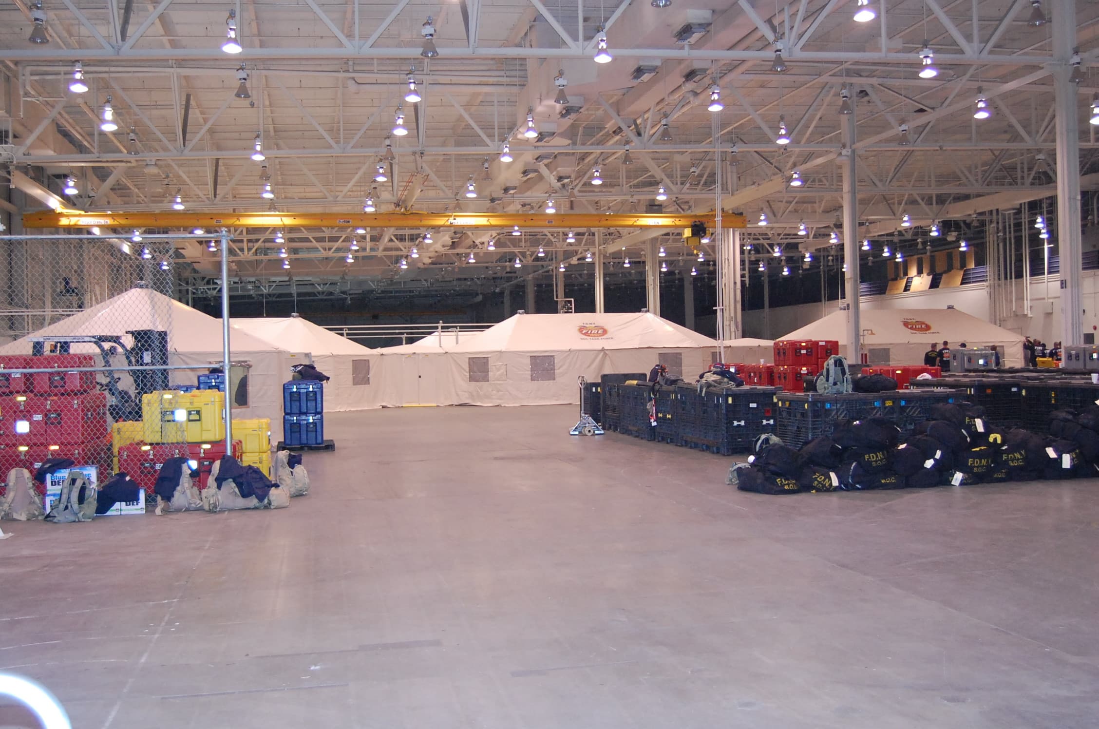 Tan tents, stacked equipment and supply pallets set up inside a large warehouse.