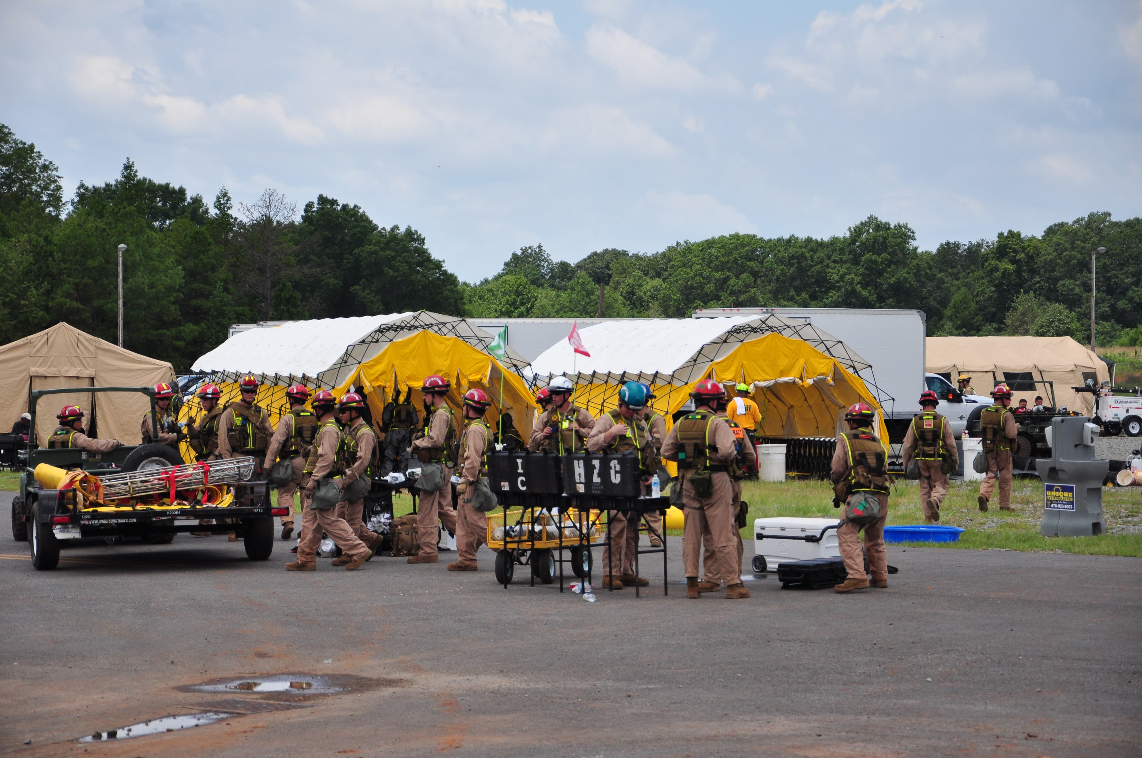 A rescue team in helmets and harnesses gathers with equipment in front of yellow and white tents at a staging area.