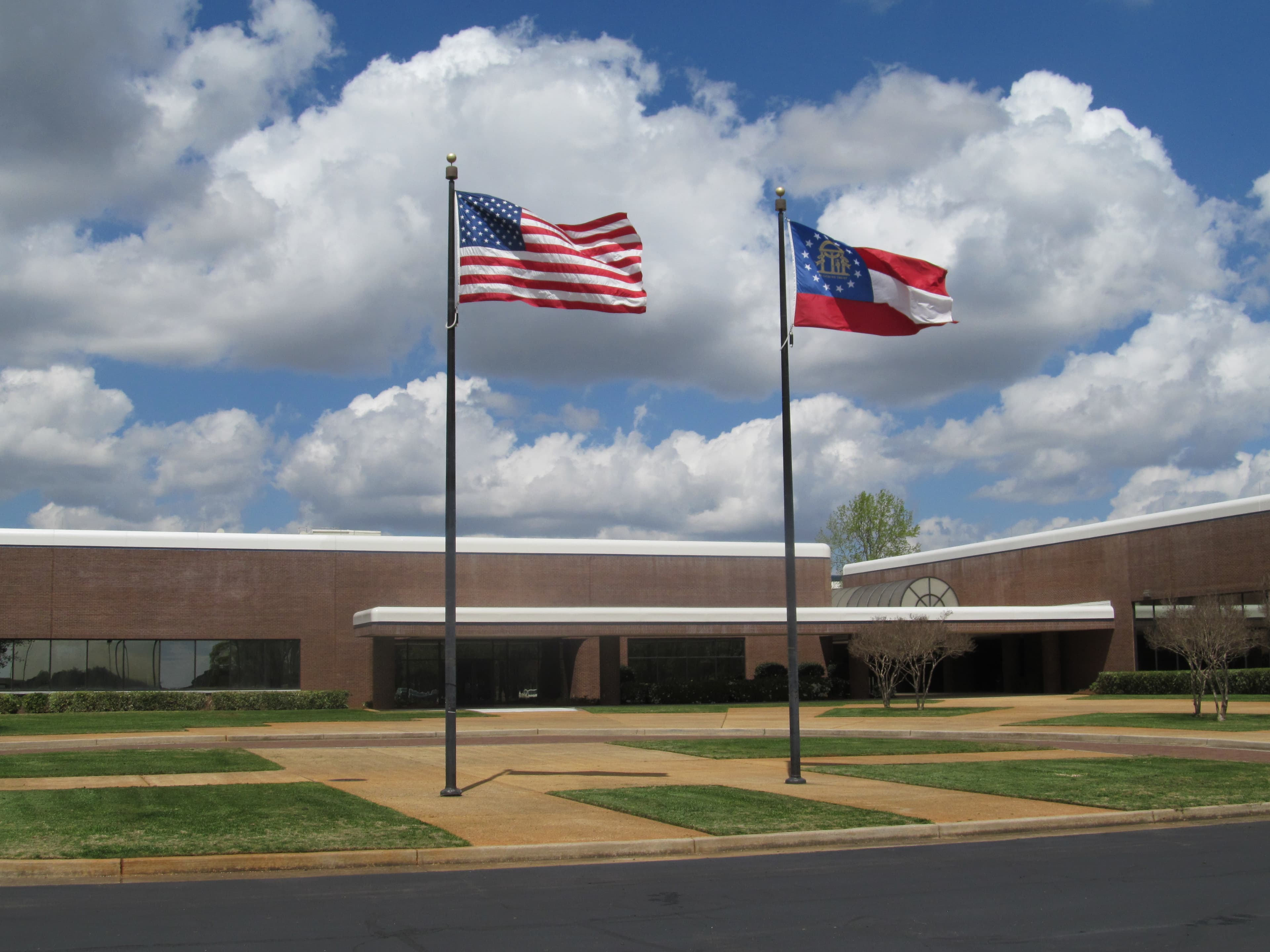 The United States and Georgia flags fly in front of the Guardian Centers brick headquarters building under a blue sky.
