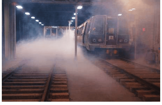 Two subway cars stand on the tracks inside the commuter rail tunnel as smoke fills the space under the overhead lights.