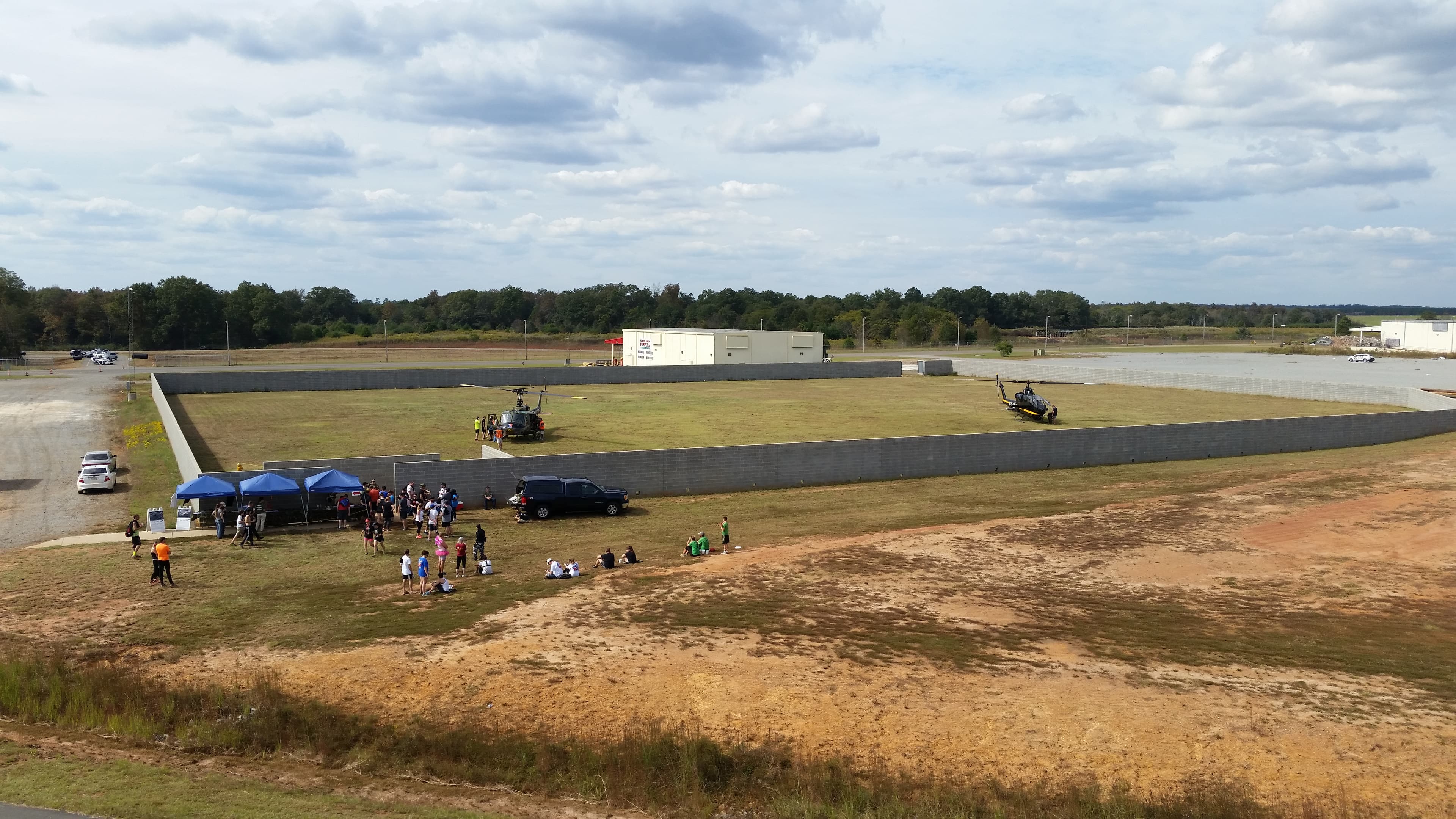 Aerial view of a walled staging area where a helicopter is parked and a group gathers under canopies.