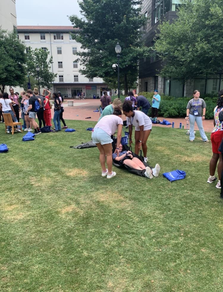 Students kneel over a classmate lying on the grass, practising patient assessment during a training session.